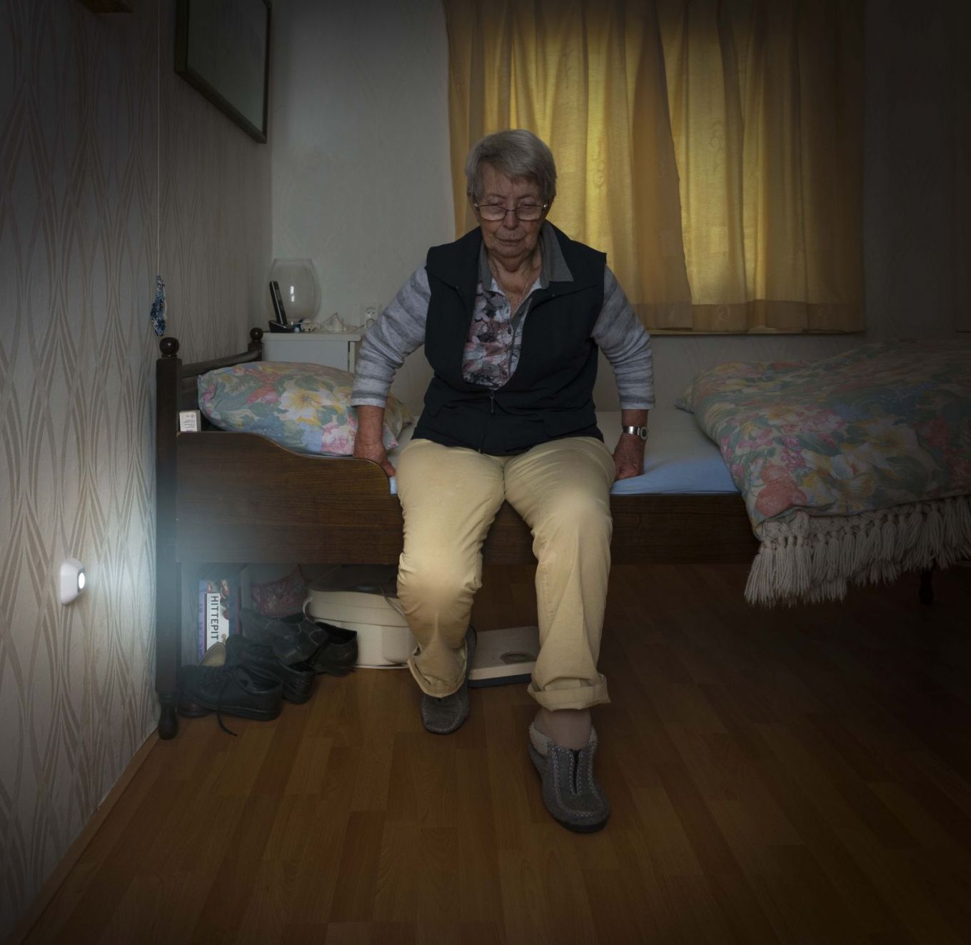 Oudere vrouw zit op rand van het bed terwijl een sensorlampje de vloer verlicht