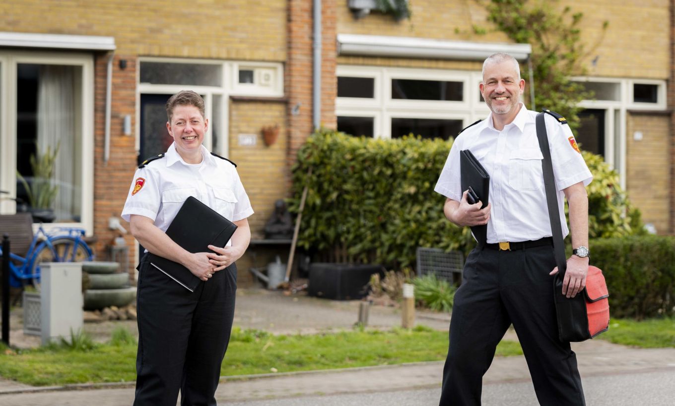 Brandweerman en brandweervrouw staan voor een huis met tablet inde hand