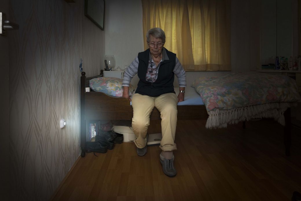 Foto van oudere vrouw die een automatisch lichtje naast haar bed activeert met haar voet